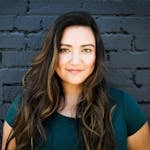 A captivating portrait of a woman smiling confidently in front of a brick wall, showcasing her long brunette hair and vibrant eyes.